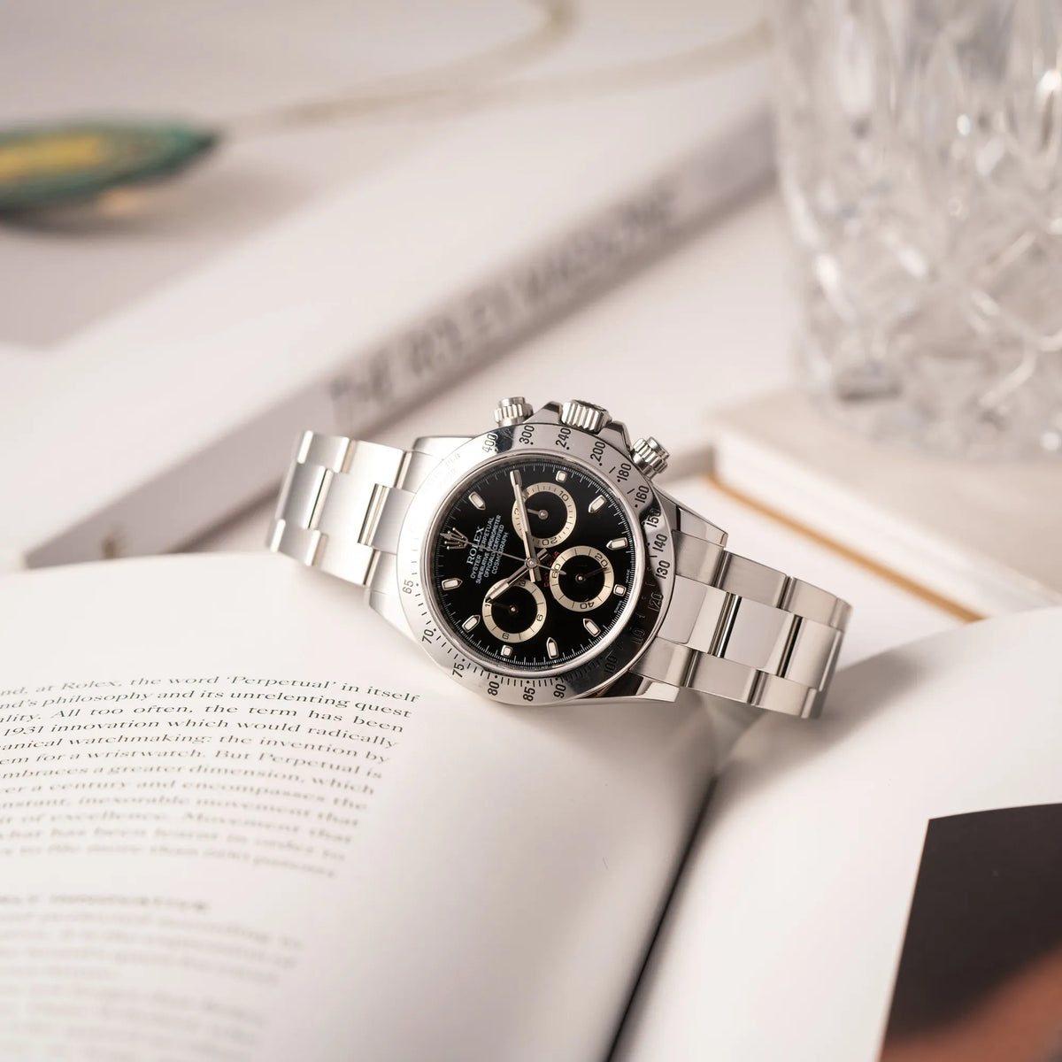 Produktoftografie der seitlich auf dem Uhrengehäuse liegenden Rolex Cosmograph Daytona 116520 mit schwarzem Zifferblatt und der klassischen Edelstahl-Lünette vor Umstellung auf die Keramik-Lünette