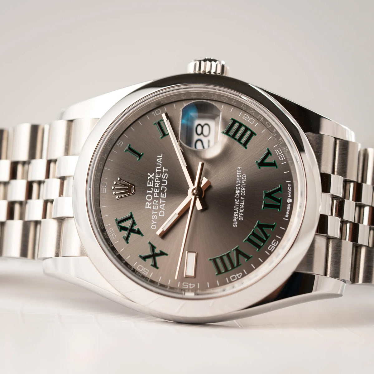 Detailaufnahme der seitlich auf dem Uhrengehäuse liegenden  Rolex Datejust 36 Wimbledon der Referenz  126200 mit glatter Lünette, anthrazitfarbenem Zifferblatt und schwarz-grünen, römischen Indizes am Jubillee-Armband