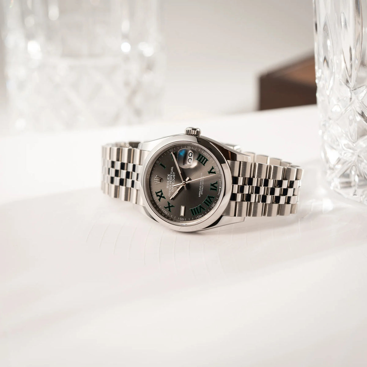 Produktfotografie der seitlich auf dem Uhrengehäuse liegenden Rolex Datejust 36 Wimbledon der Referenz 126200 mit glatter Lünette, anthrazitfarbenem Zifferblatt und schwarz-grünen, römischen Indizes am Jubillee-Armband