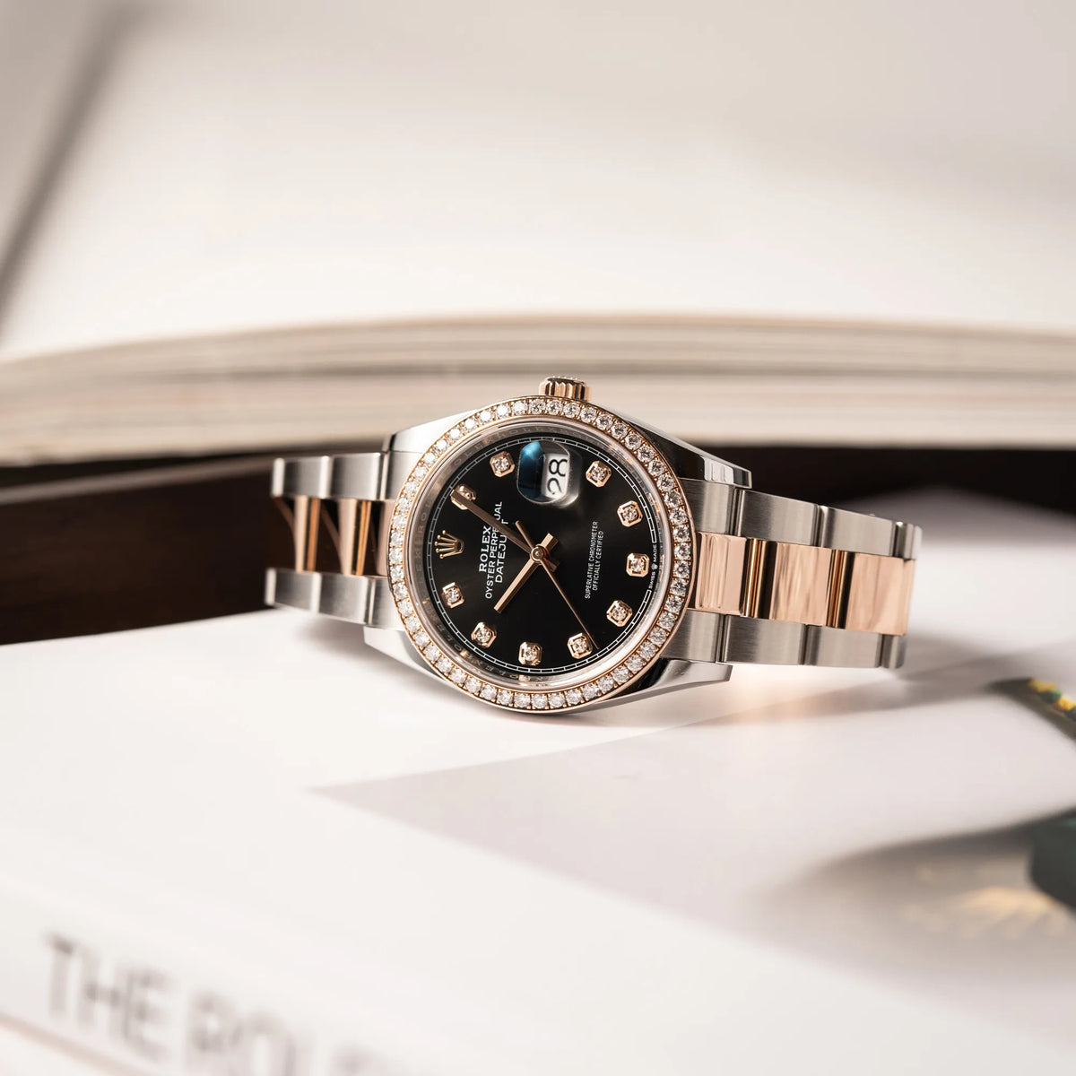 Rolex Datejust 36 126218RBR in Stahl-Roségold mit schwarzem Diamant-Zifferblatt und Diamant-Lünette im Factory-Besatz liegt auf einem Rolex-Magazin
