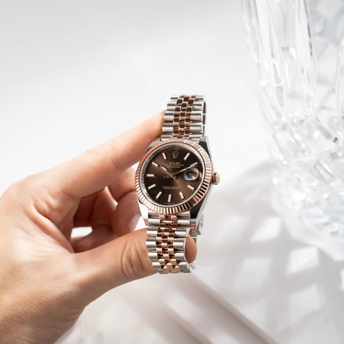 Mann hält die bicolor Rolex Datejust 41 der Referenz 126331 Chocolate in Stahl-Roségold mit einem zum Roségold passenden braunen Zifferblatt am zugehörigen Jubilee-Armband in seiner Hand und präsentiert die Uhr in die Kamera