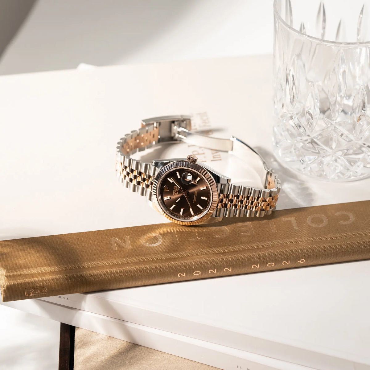Produktfotografie der bicolor Rolex Datejust 41 der Referenz 126331 Chocolate in Stahl-Roségold mit einem zum Roségold passenden braunen Zifferblatt am zugehörigen Jubilee-Armband, während die Uhr auf einem Buch liegt