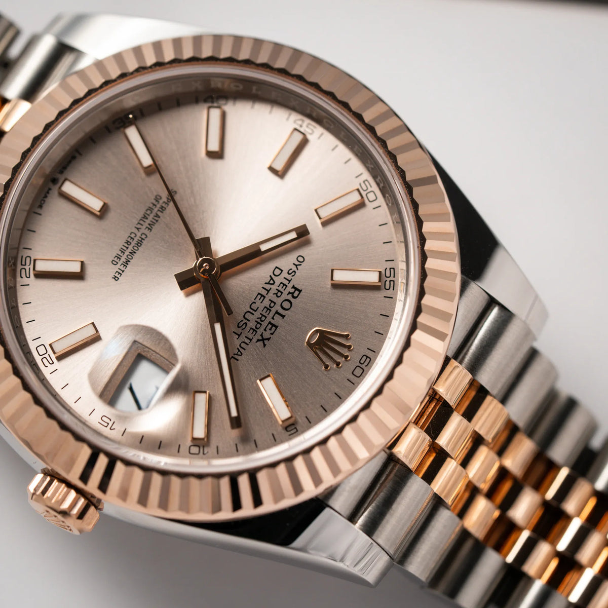 Nahaufnahme der Rolex Datejust 41 in Stahl-Roségold mit am passenden Jubilee-Armband mit dem pink-lachsfarbenen "Sundust" Zifferblatt mit Fokus auf der Rolex Krone bei 12 Uhr
