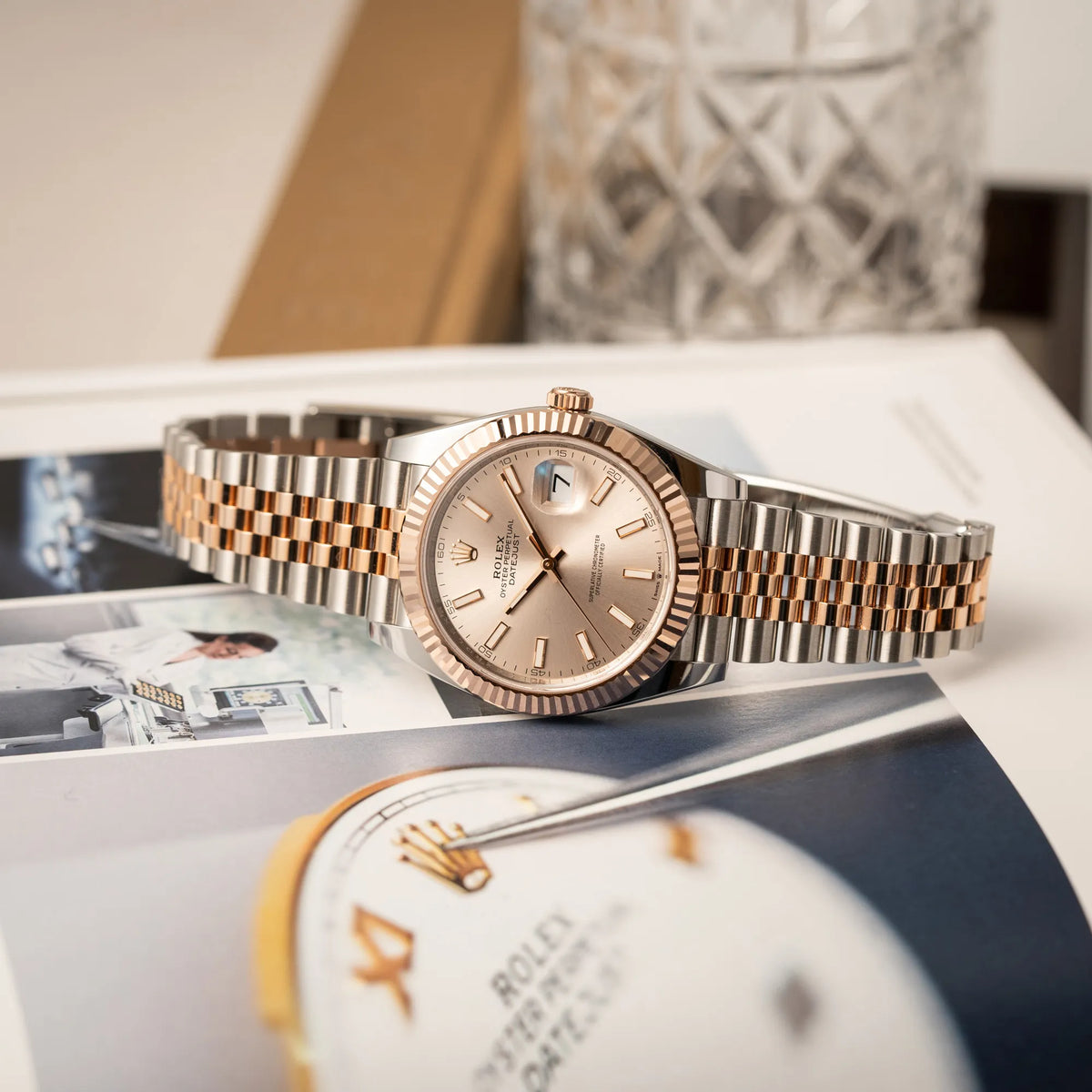 Rolex Datejust 41 in Stahl-Roségold mit am passenden Jubilee-Armband mit dem pink-lachsfarbenen "Sundust" Zifferblatt liegt seitlich auf dem Uhrengehäuse