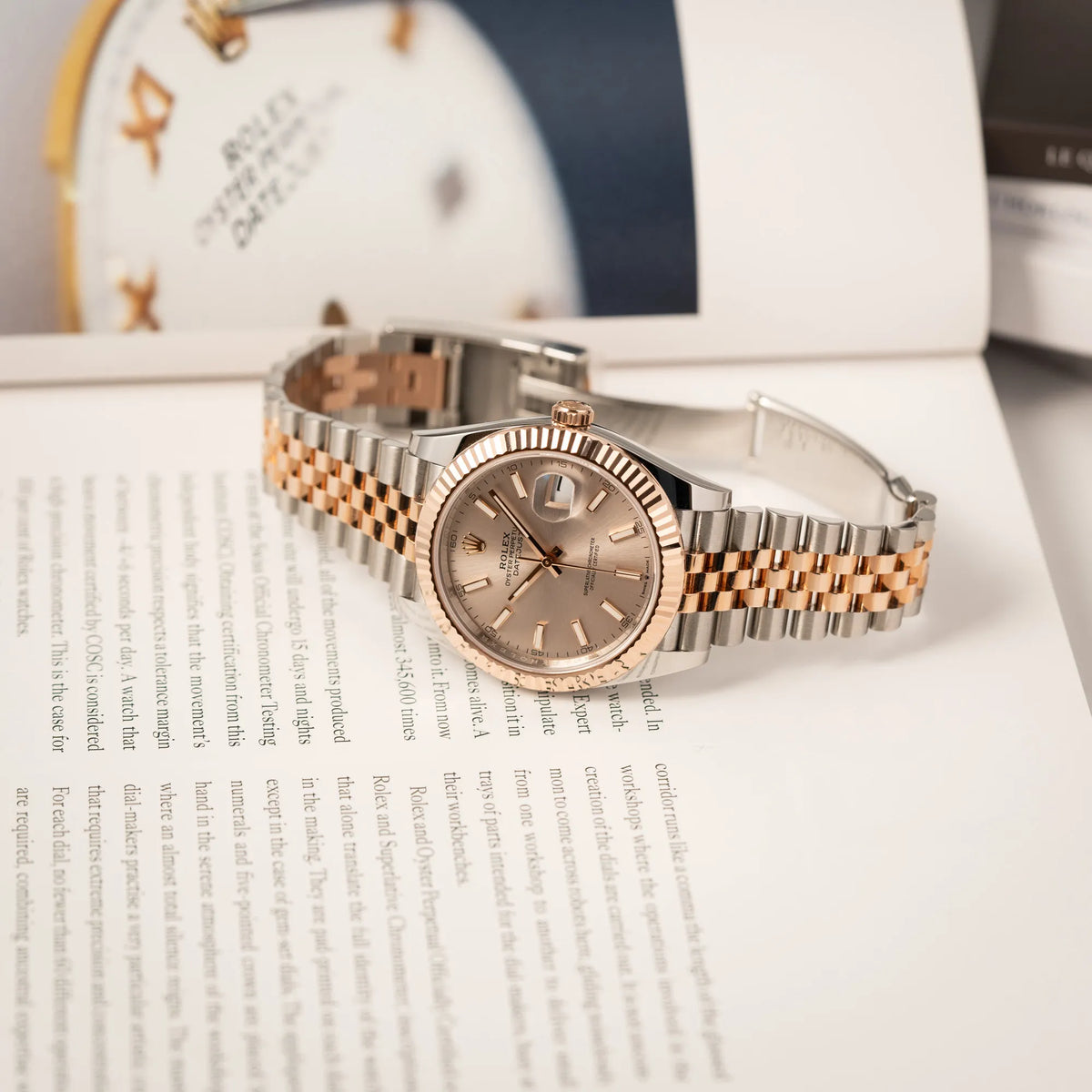 Rolex Datejust 41 in Stahl-Roségold mit am passenden Jubilee-Armband mit dem pink-lachsfarbenen "Sundust" Zifferblatt liegt mit geöffneter Faltschliesse auf einem Buch