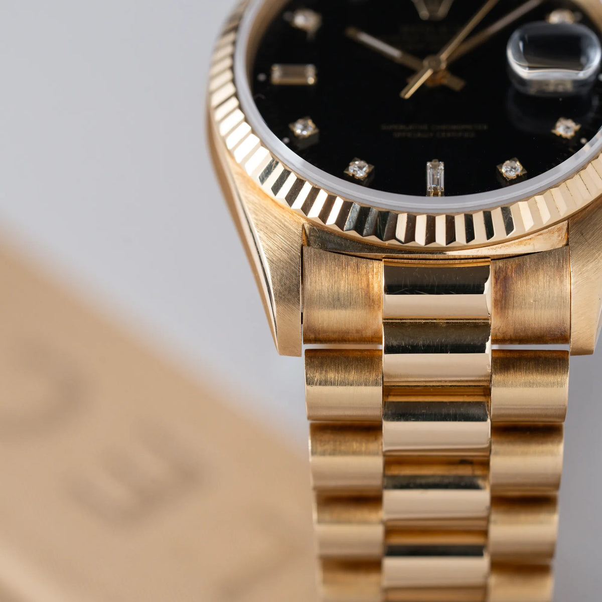 Produktfotografie der Rolex Day-Date 36 in Gelbgold mit der Referenznummer 18238 mit englischer Tagesanzeige, mit schwarzem Lack-Zifferblatt und Diamant-Indizes mit Fokus auf dem President-Armband und dessen Patina