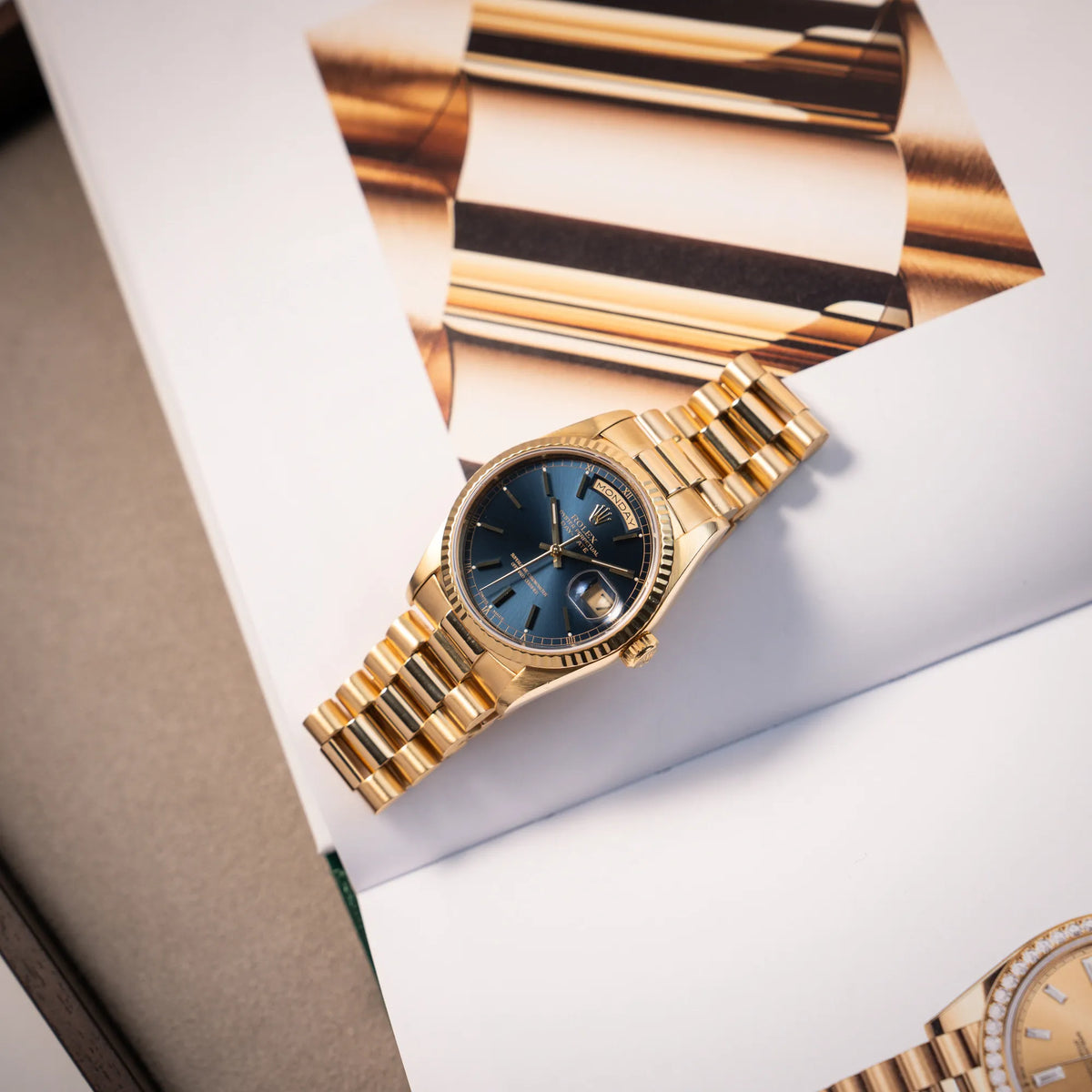Fotografie der gelbgoldenen Rolex Day-Date 36 der Referenz 18238 mit blauem Zifferblatt und englisch-sprachiger Tagesanzeige mit Rolex-Katalog als Hintergrund