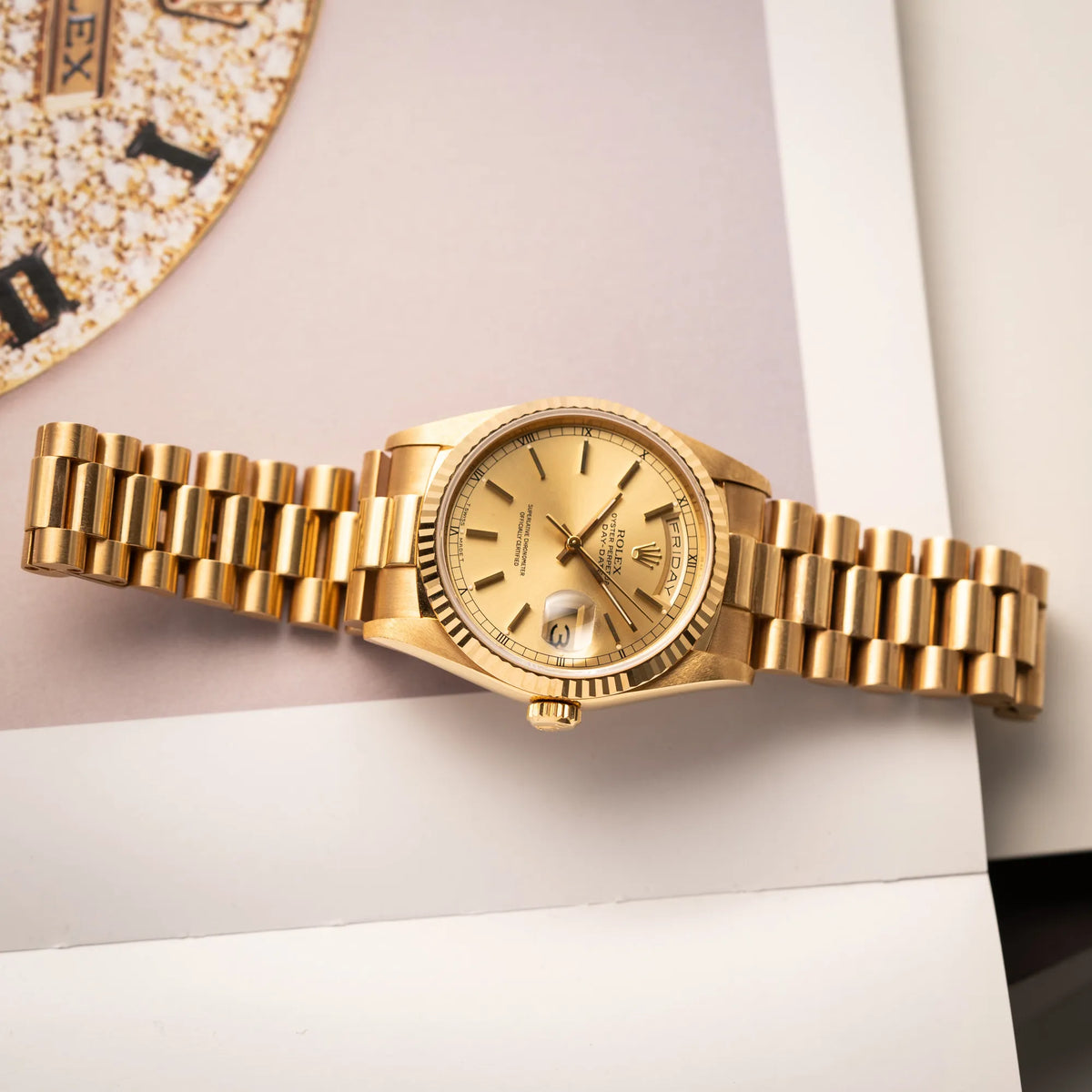 Produktfotografie der flach auf einem Buch liegenden Rolex Day-Date 36 der Referenz 18238 in Gelbgold mit champagnerfarbenem Stick-Dial