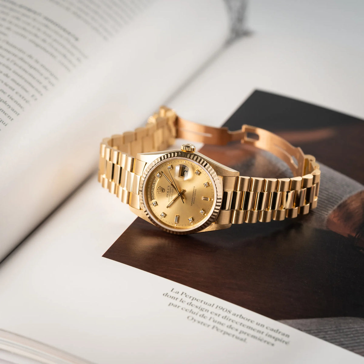 Rolex Day-Date 36 in Gelbgold der Referenz 18238 aus 1991 mit Champagner-Diamant-Zifferblatt und englischsprachiger Tagesanzeige liegt mit geöffneter Faltschliesse auf einem Buch