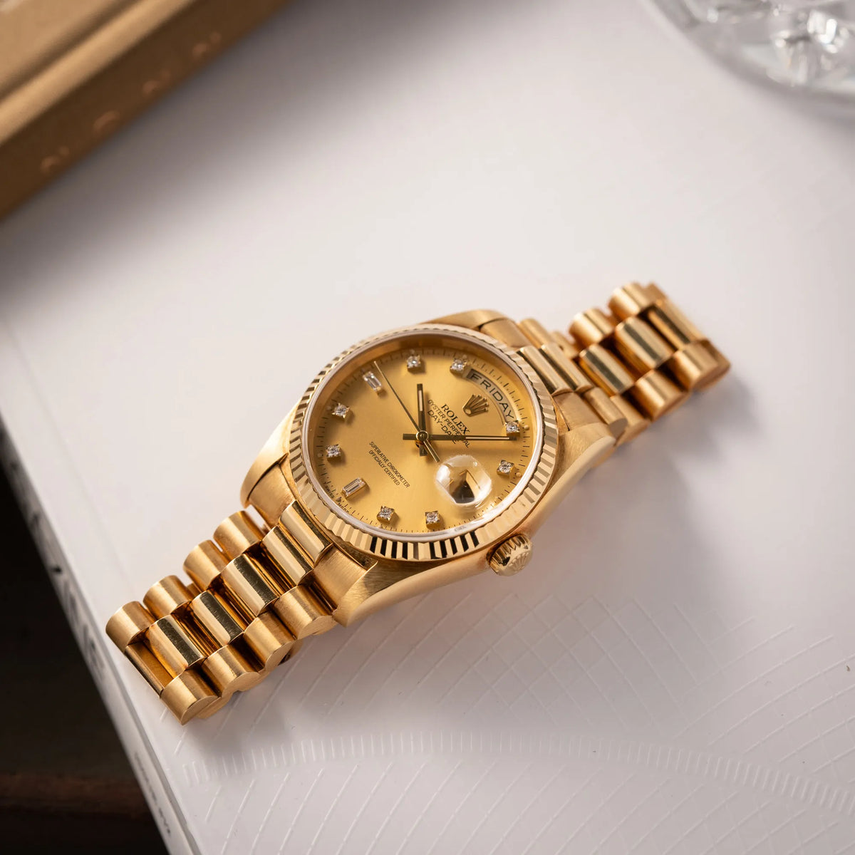 Produktfotografie der flach auf einem Buch liegenden Rolex Day-Date 36 der Referenz 18238 mit champagnerfarbenem Diamant-Zifferblatt