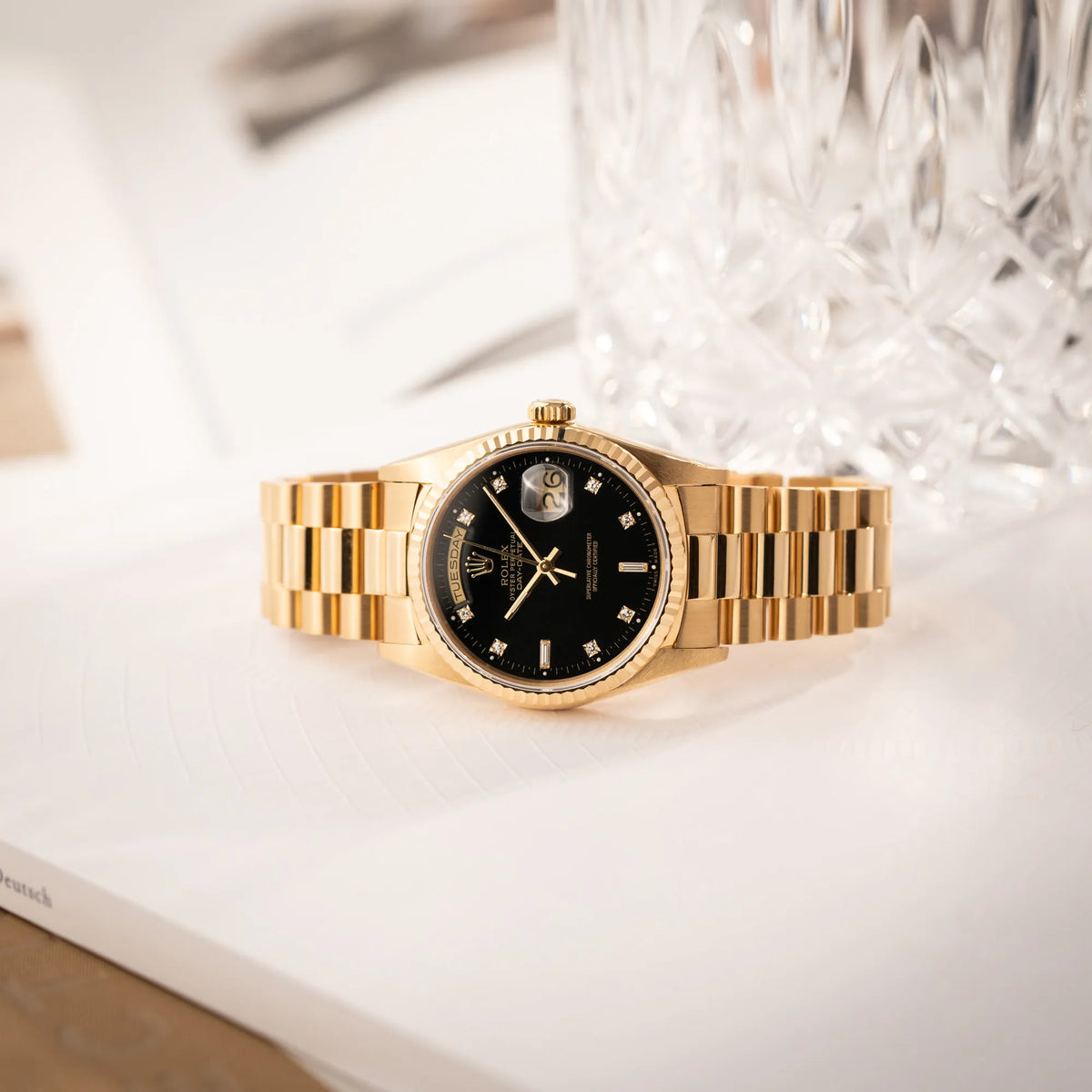 Rolex Day-Date 36 der Referenz 18238 in Gelbgold mit schwarzen Diamond-Dial am President-Armband liegt seitlich auf dem Uhrengehäuse