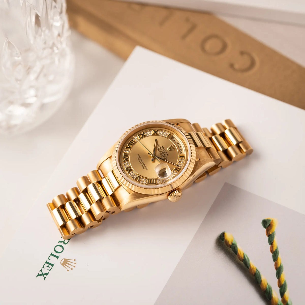 Gelbgoldene Rolex Day-Date 36 der Referenz 18238 mit einem seltenen Myriad-Dial mit Diamant-Kranz und römischen Indizes liegt flach auf einem Rolex-Uhrenbuch