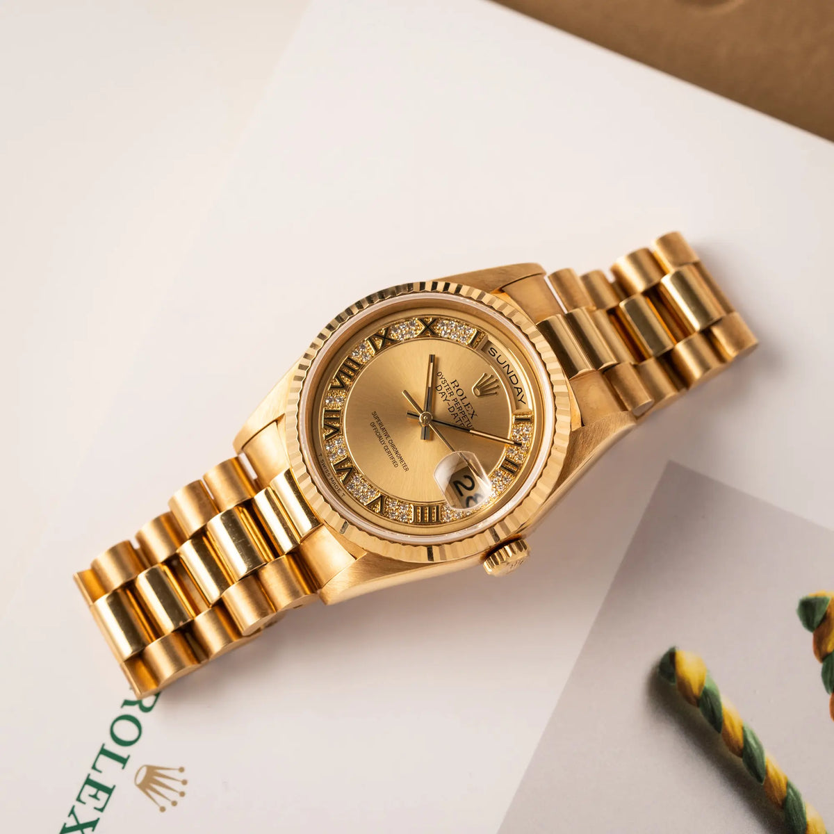 Gelbgoldene Rolex Day-Date 36 der Referenz 18238 mit einem seltenen Myriad-Dial mit Diamant-Kranz und römischen Indizes liegt flach auf einem Buch über Rolex-Uhren