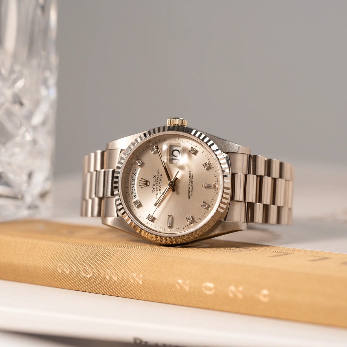 Produktfotografie der seitlich auf dem Gehäuse liegende Rolex Day-Date der Referenz 18239 in 36 mm aus 18 karätigem Weißgold mit silbernem Diamant-Zifferblatt