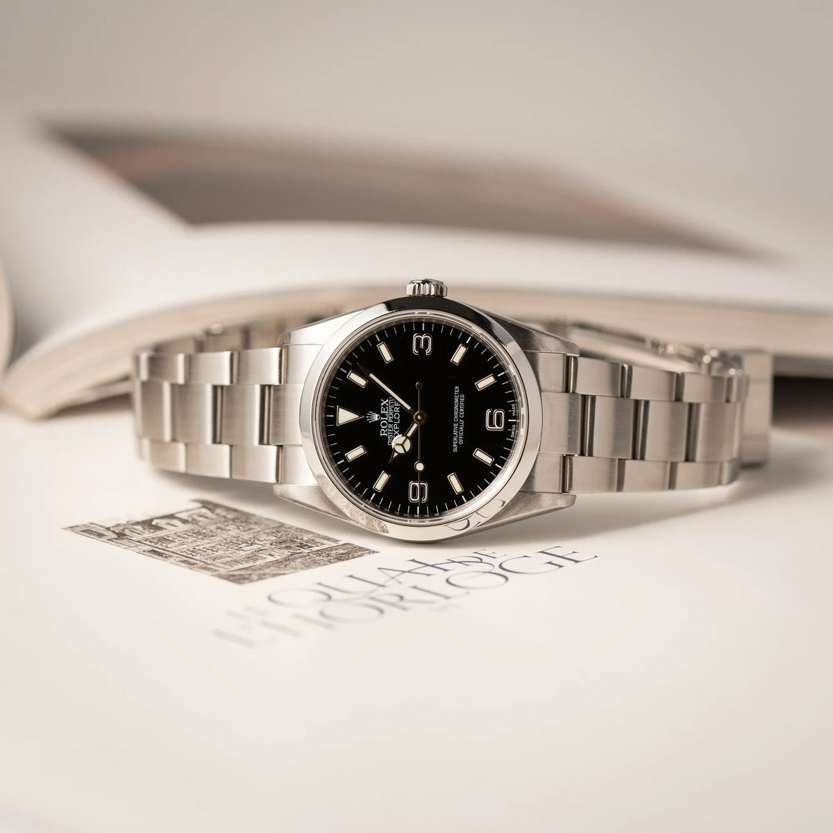 Rolex Explorer 36 der Referenz 114270 mit dem klassischen schwarzen 3-6-9 Zifferblatt liegt auf der seitlichen Gehäuseflanke der Produktfotografie der Rolex Explorer 36 der Referenz 114270 mit dem klassischen schwarzen 3-6-9 Zifferblatt