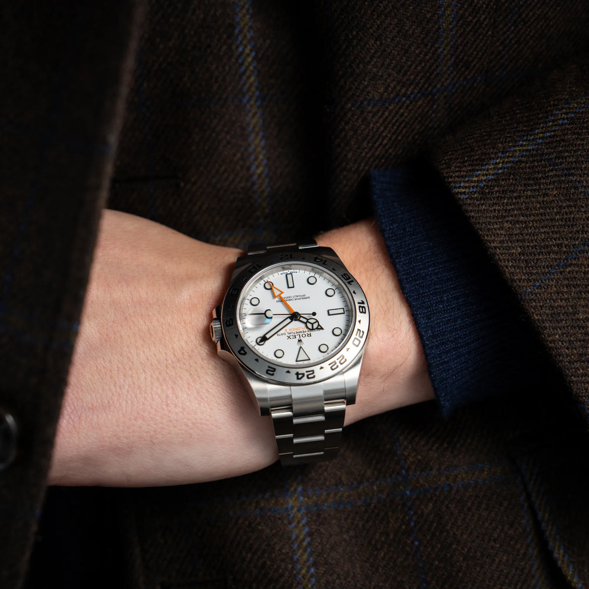 Mann in braunem Sakko trägt die Rolex Explorer II 216570 aus 2021 mit dem weißen Polar Zifferblatt mit dem typischen orangen GMT-Zeiger in einem sehr guten Zustand