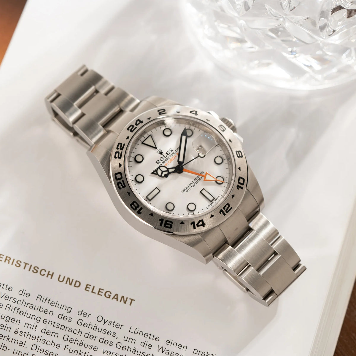 Produktfotografie der Rolex Explorer II 216570 aus 2021 mit dem weißen Polar Zifferblatt mit dem typischen orangen GMT-Zeiger in einem sehr guten Zustand, während diese flach auf dem Uhrenband liegt