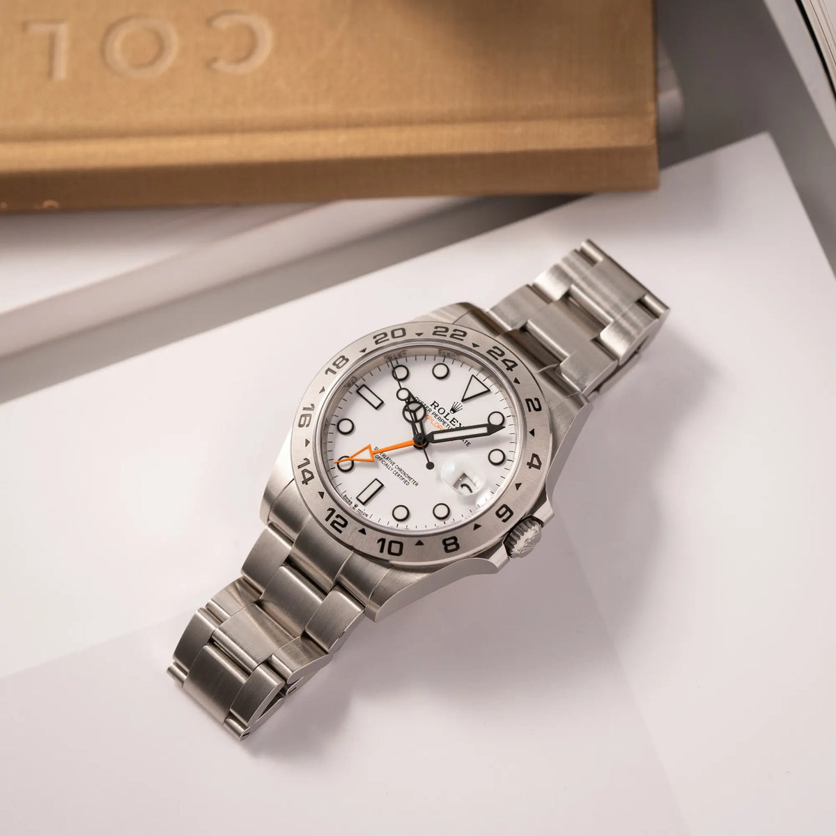 Rolex Explorer II der Referenz 226570 am Oyster-Stahlband mit dem weißen Polar-Zifferblatt und dem typischen orangen 24-Stunden-Zeiger liegt flach auf einem Uhrenbuch