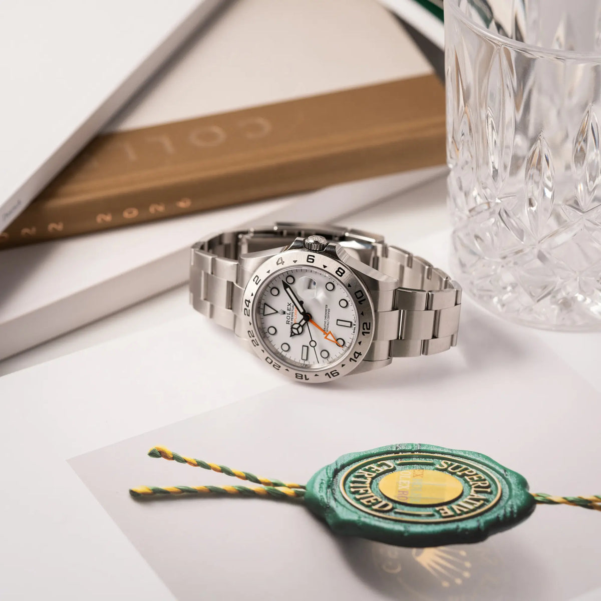 Rolex Explorer II der Referenz 226570 am Oyster-Stahlband mit dem weißen Polar-Zifferblatt und dem typischen orangen 24-Stunden-Zeiger liegt seitlich auf einem Uhrenbuch