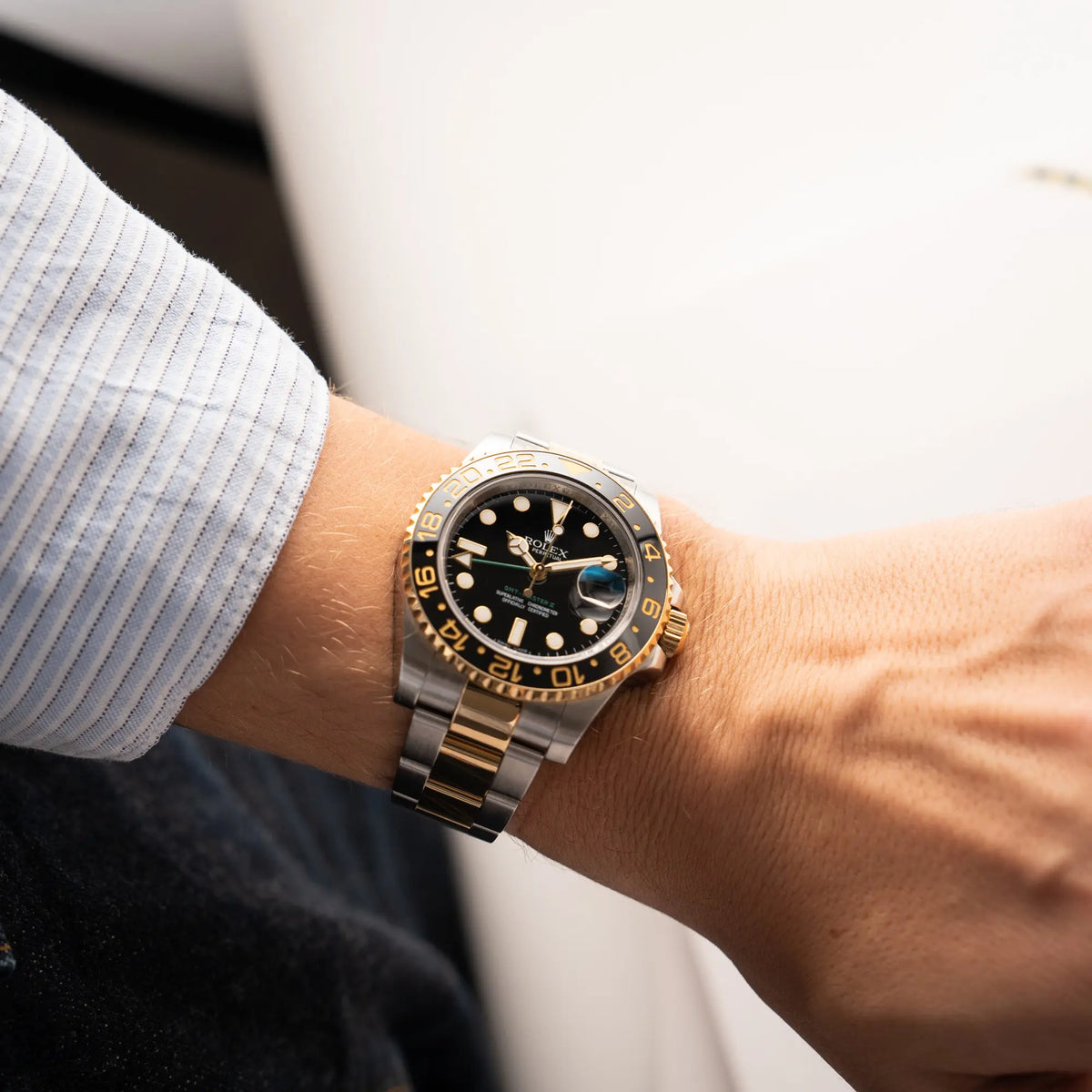 Mann in hellblauem Hemd trägt die Rolex GMT-Master II der Referenz 116713LN in Stahl-Gold mit schwarzem Zifferblatt und dem grünen GMT-Zeiger an seinem handgelenk