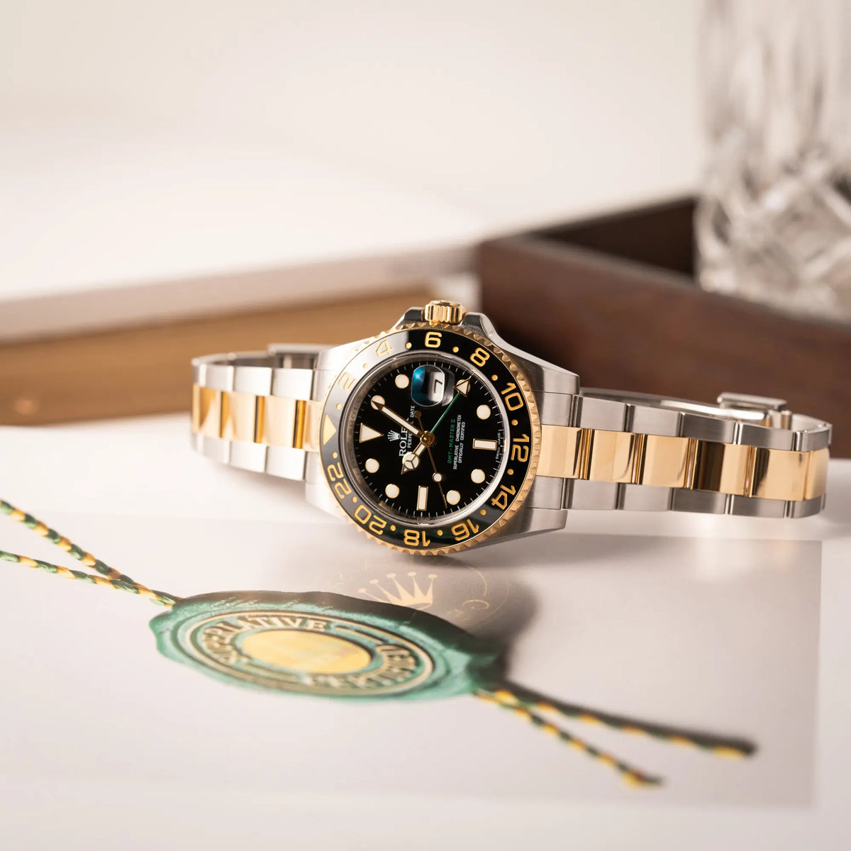 Produktfotografie der auf dem seitlichen Gehäuse liegenden Rolex GMT-Master II der Referenz 116713LN in Stahl-Gold mit schwarzem Zifferblatt und dem grünen GMT-Zeiger 