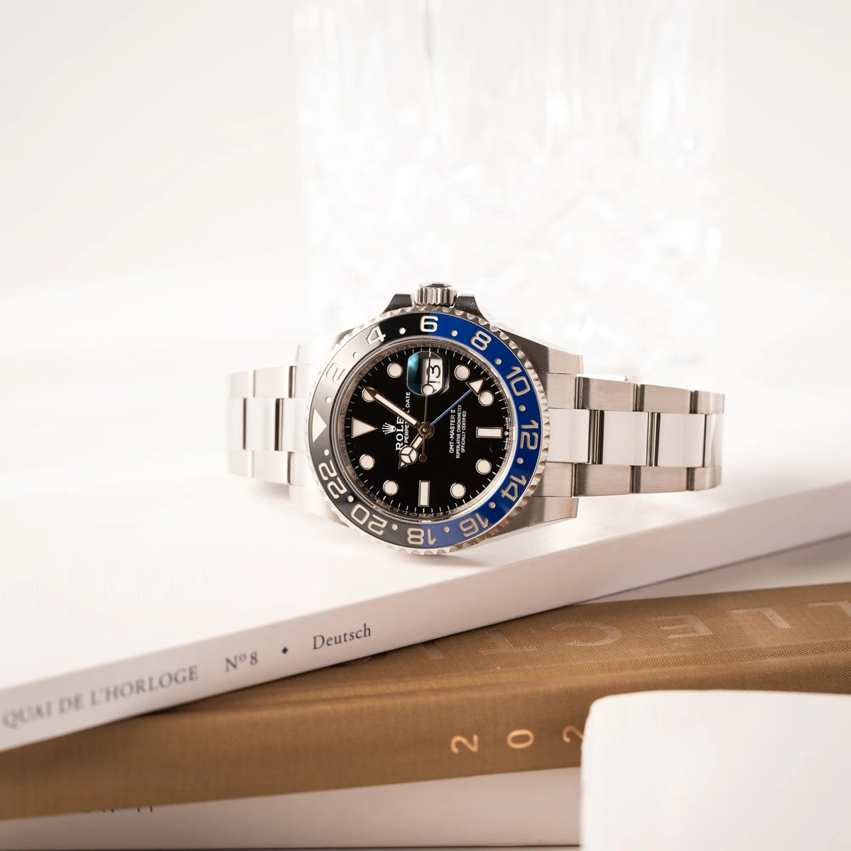 Rolex GMT-Master II 126710BLNR mit dem Nickname Batman und der typischen Kombination aus blau-schwarzer Keramik-Lünette und schwarzem Zifferblatt liegt seitlich auf einem Stapel mit Uhrenbüchern