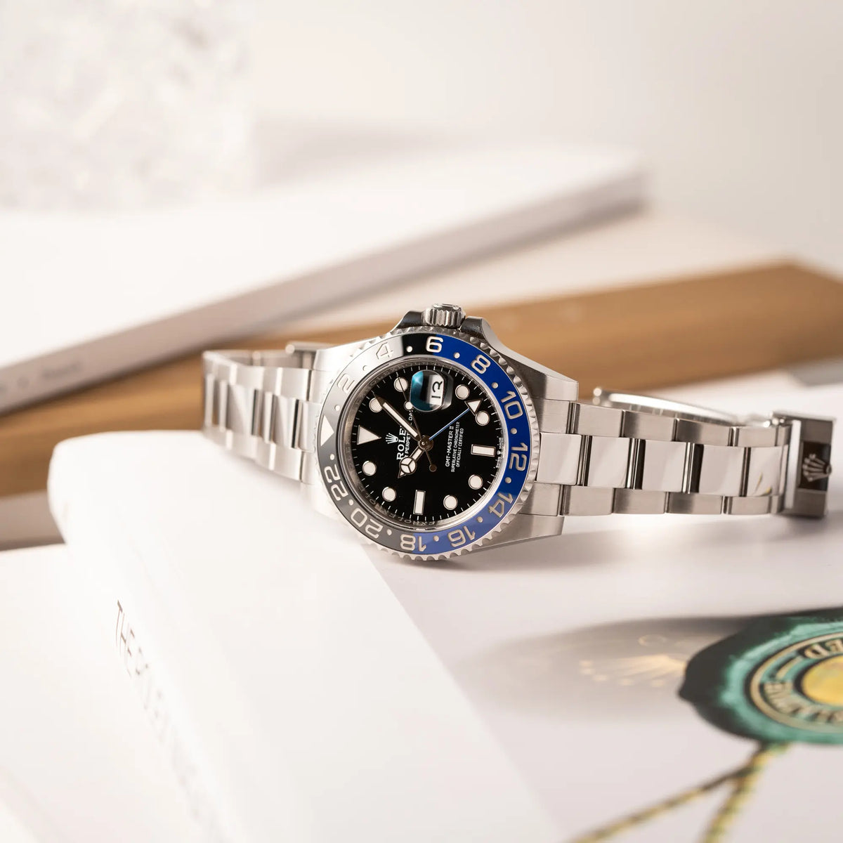Produktfotografie der auf einem Uhrenbuch liegenden Rolex GMT-Master II 126710BLNR mit dem Nickname Batman und der typischen Kombination aus blau-schwarzer Keramik-Lünette und schwarzem Zifferblatt