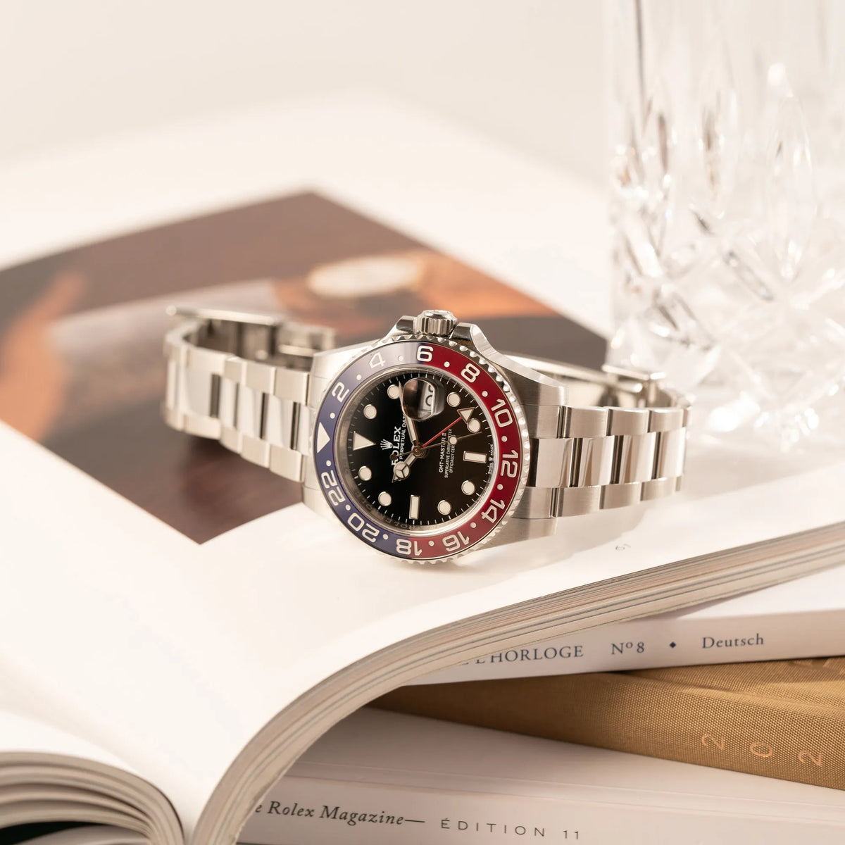 Produktfotografie zeigt die seitlich auf dem Uhrengehäuse liegenden Rolex GMT-Master II der Referenz 126710BLRO mit der blau-roten Pepsi-Lünette in Keramik am Oyster-Stahl-Armband im ungetragenen Zustand