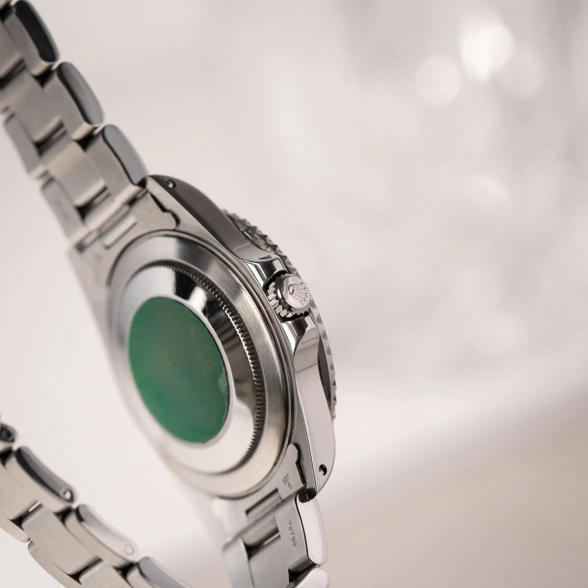 Produktfotografie der Rolex GMT-Master II der Referenz 16710  2000 mit  schwarz-roter Coke-Lünette und dem für das Jahr 2000 typische "Swiss Only" - Zifferblatt zeigt den Gehäuseboden mit grünem original Sticker und die Aufzugskrone