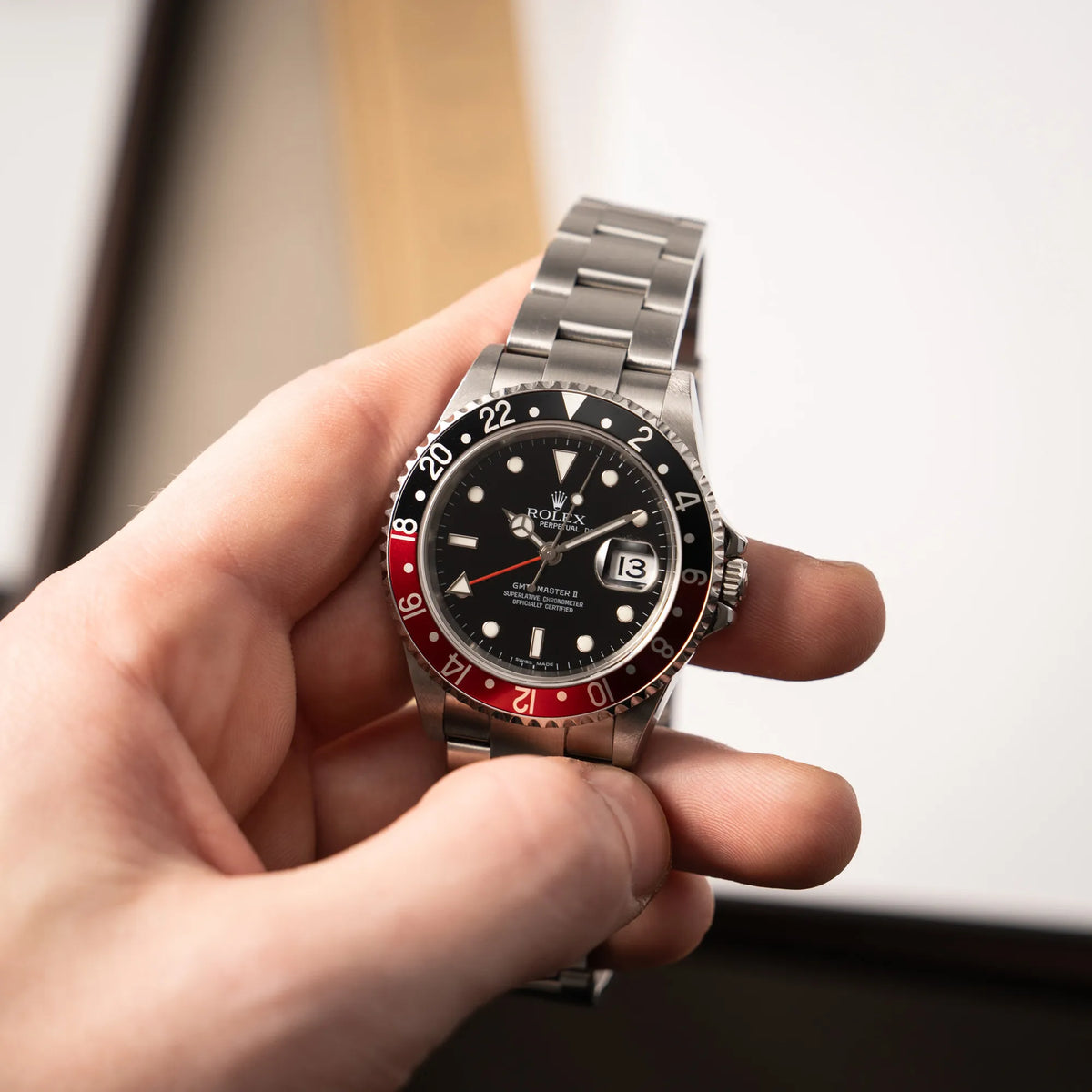 Mann hält die Rolex GMT-Master II der Referenz 16710 mit der schwarz-roten "Coke"-Lünette aus 2007 mit dem "No-Hole"-Uhrengehäuse in seiner Hand und präsentiert die Uhr in die Kamera