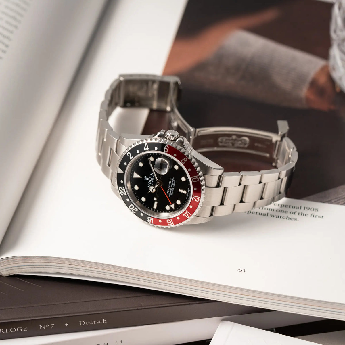 Ptoduktfotografie der Rolex GMT-Master II der Referenz 16710 mit der schwarz-roten "Coke"-Lünette aus 2007 mit dem "No-Hole"-Uhrengehäuse liegt auf einem Uhrenmagazin