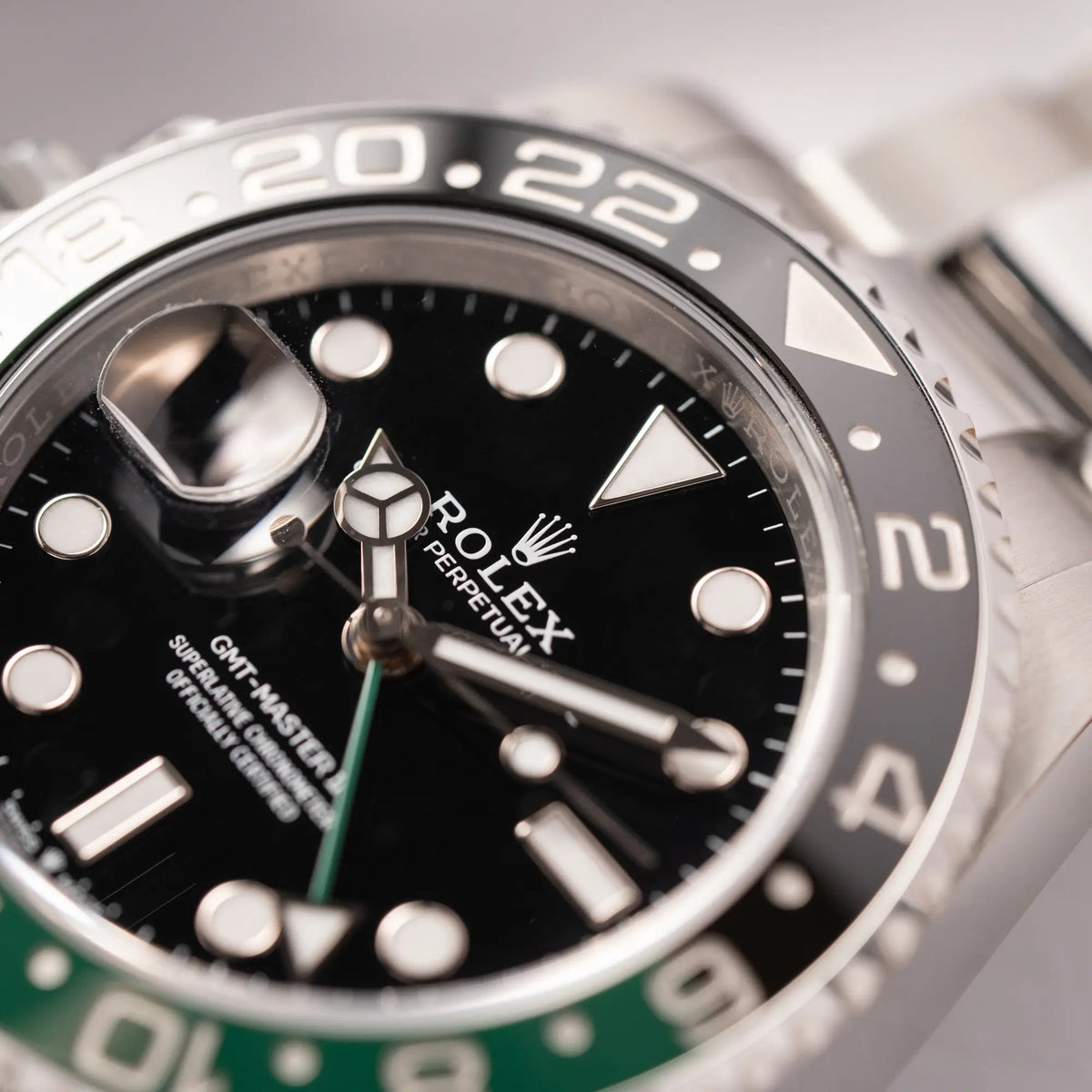 Detailaufnahme zeigt den Zeigersatz der Rolex GMT-Master II der Referenz 126720VTNR mit dem Nickname "Sprite" mit einer schwarz-grünen Keramik-Lünette am Oyster-Stahlband im neuwertigen Zustand, mit der Besonderheit der links liegenden Aufzugskrone, so dass Linkshänder die Uhr an der rechten Hand tragen können