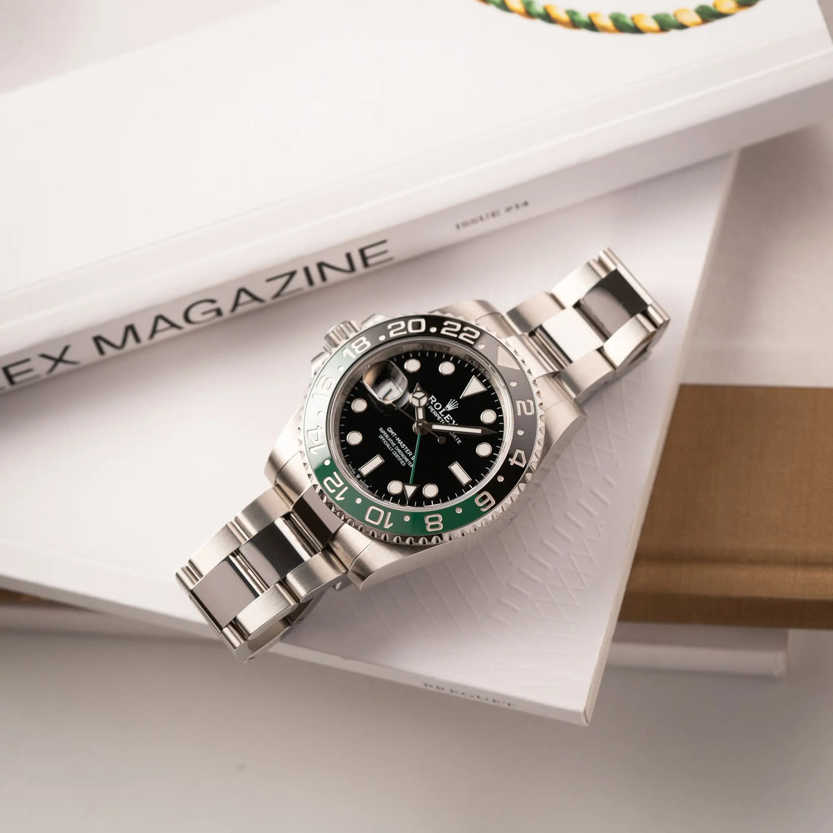 Rolex GMT-Master II der Referenz 126720VTNR mit dem Nickname "Sprite" mit einer schwarz-grünen Keramik-Lünette am Oyster-Stahlband im neuwertigen Zustand, mit der Besonderheit der links liegenden Aufzugskrone, so dass Linkshänder die Uhr an der rechten Hand tragen können liegt flach auf einem Uhrenmagazin