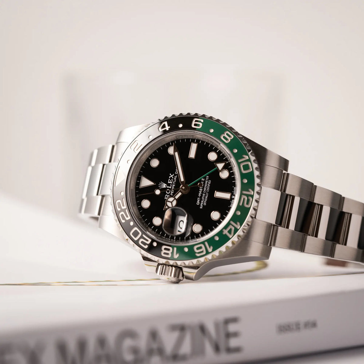 Produktfotografie der Rolex GMT-Master II der Referenz 126720VTNR mit dem Nickname "Sprite" mit einer schwarz-grünen Keramik-Lünette am Oyster-Stahlband im neuwertigen Zustand, mit der Besonderheit der links liegenden Aufzugskrone, so dass Linkshänder die Uhr an der rechten Hand tragen können, die seitlich auf der Aufzugskrone aufliegt