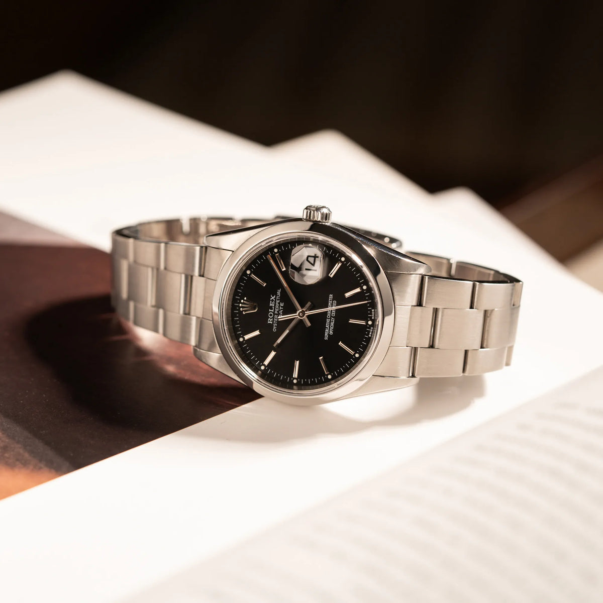 Rolex Oyster Perpetual 34 mit schwarzem Zifferblatt der Referenz 15200 mit glatter Lünette und 34mm Gehäusedurchmesser liegt seitlich auf dem Uhrengehäuse