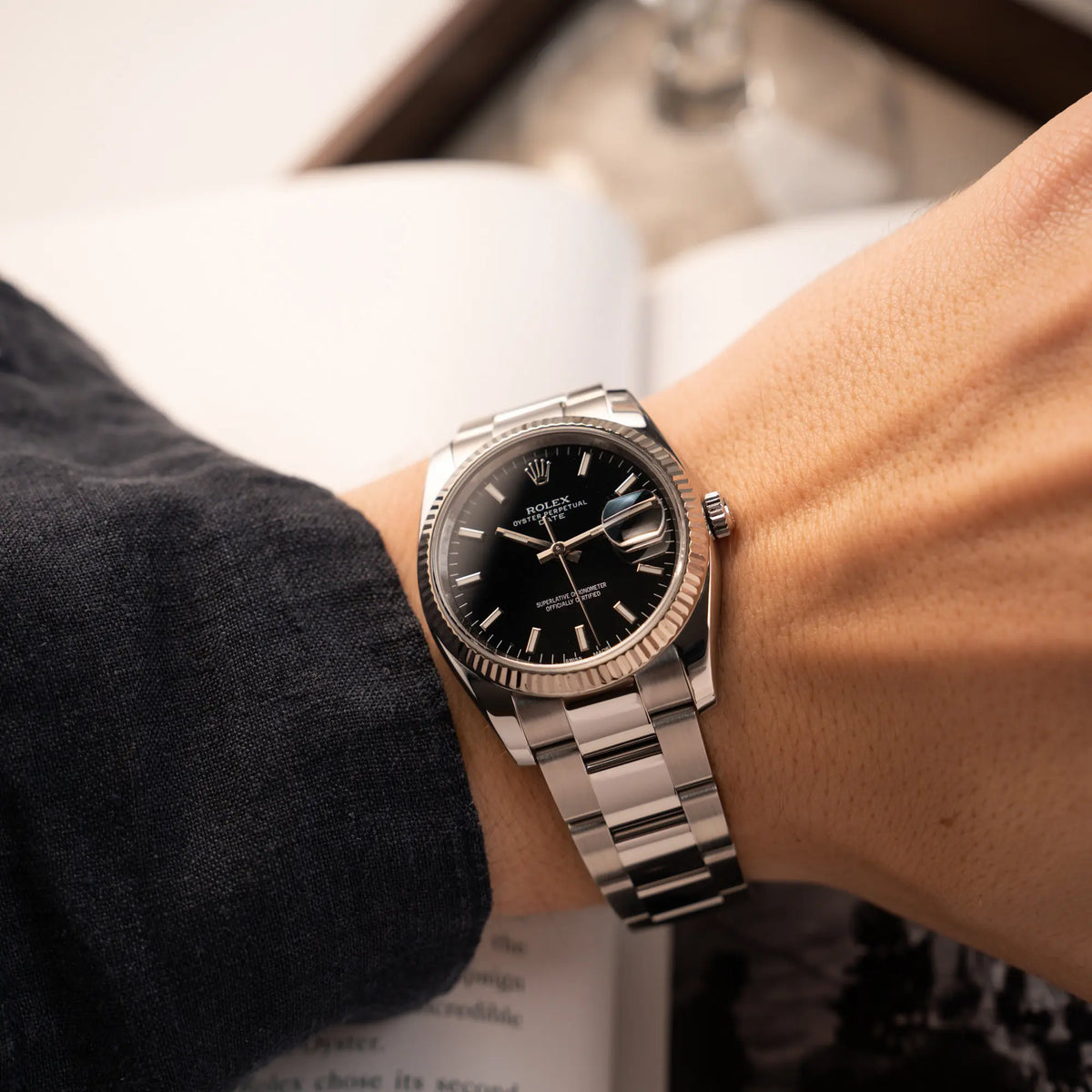Mann trägt die Rolex Oyster Perpetual Date 34 der Referenz 115234 mit schwarzem Zifferblatt und der geriffelten Weißgold-Lünette an seinem Arm