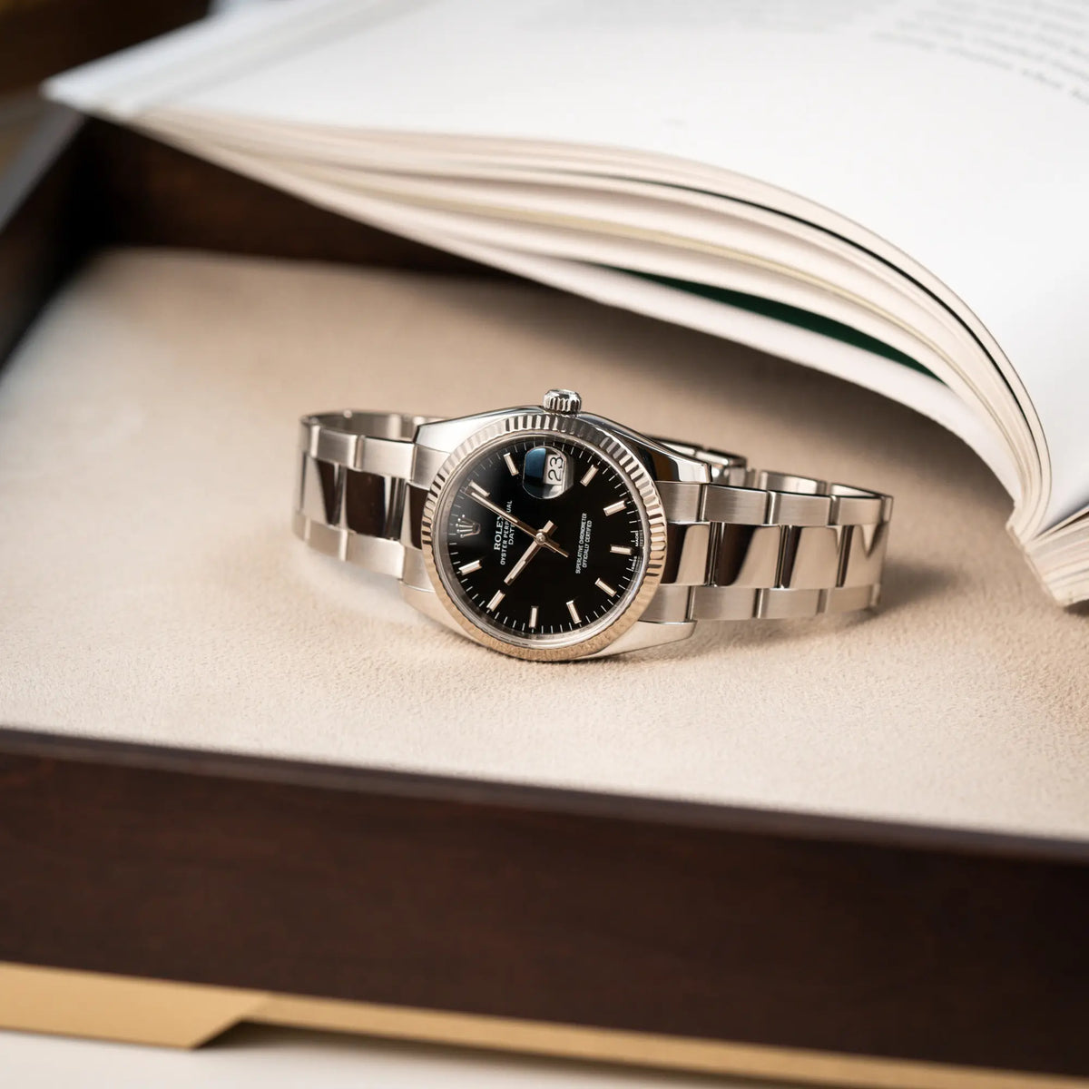 Produktfotografie als Titelbild für die Rolex Oyster Perpetual Date 34 der Referenz 115234 mit schwarzem Zifferblatt und der geriffelten Weißgold-Lünette 