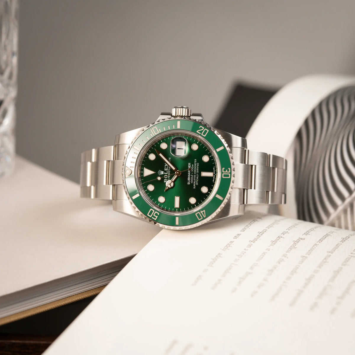 Produktfotografie der seitlich auf dem Gehäuse liegenden Rolex Submariner Date 116610LV "Hulk" mit grünem Zifferblatt und grüner Keramik-Lünette