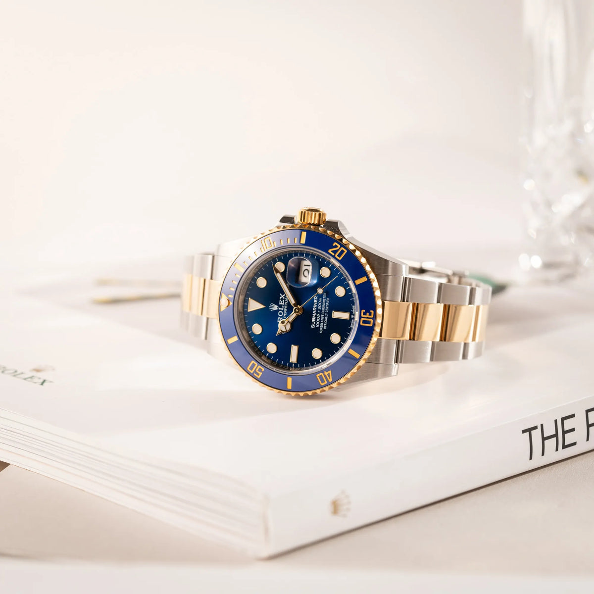 Rolex Submariner Date 126613LB Bluesy mit der typischen Kombination aus blauem Zifferblatt und Lünette mit dem Gehäuse und Armband aus Stahl-Gold leigt auf einem buch über Rolex Uhren