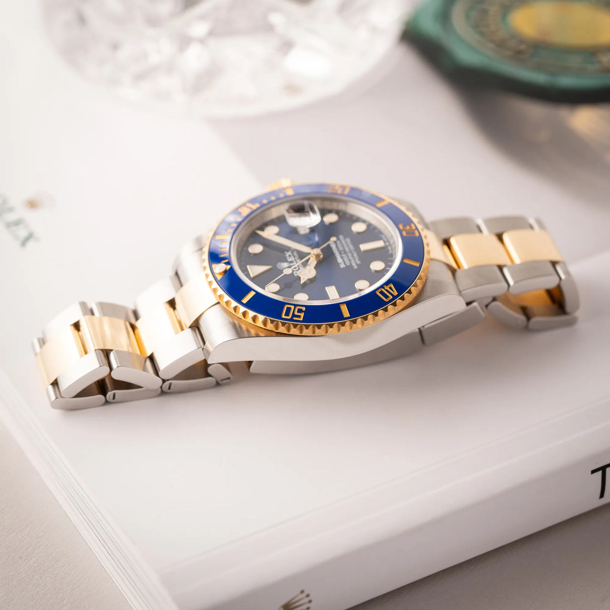 Rolex Submariner Date 126613LB Bluesy mit der typischen Kombination aus blauem Zifferblatt und Lünette mit dem Gehäuse und Armband aus Stahl-Gold liegt flach auf einem Buch über Rolex Uhren