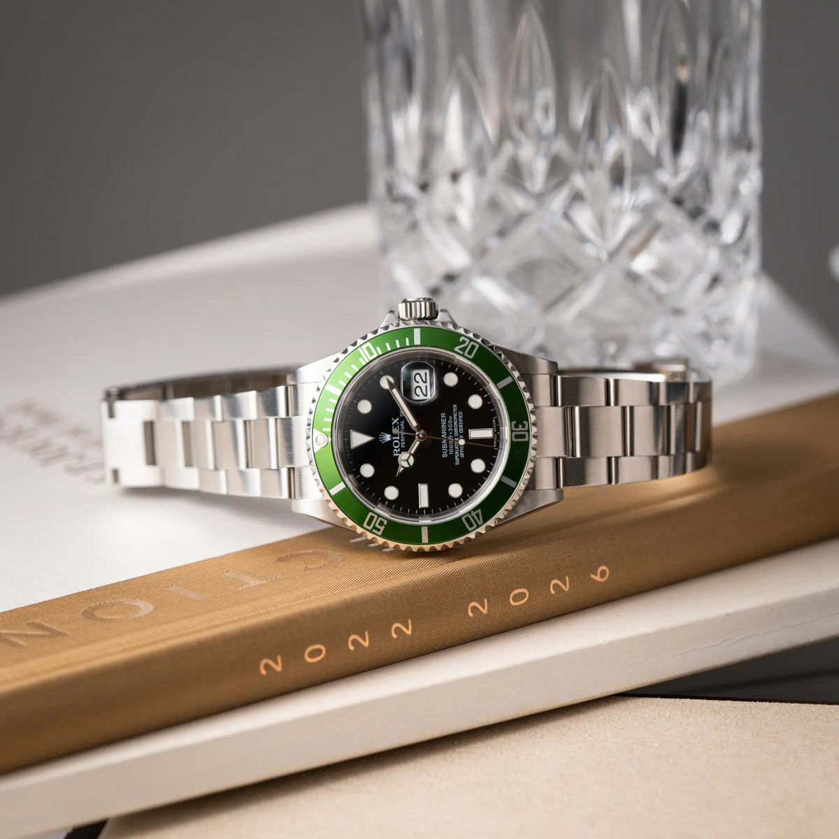 Produktfotografie der seitlich auf dem Gehäuse liegenden Rolex Submariner Date 16610LV aus 2007 mit schwarzem Zifferblatt und der grünen "Kermit" Aluminium-Lünetten-Einlage
