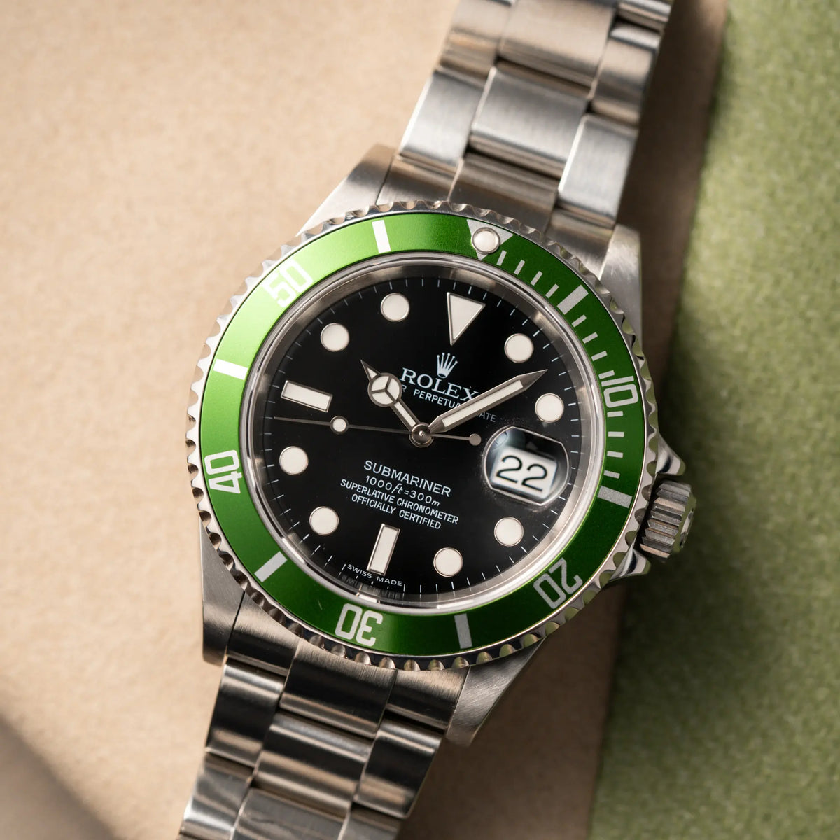Produktfotografie der flach auf dem Band liegenden Rolex Submariner Date 16610LV aus 2007 mit schwarzem Zifferblatt und der grünen "Kermit" Aluminium-Lünetten-Einlage