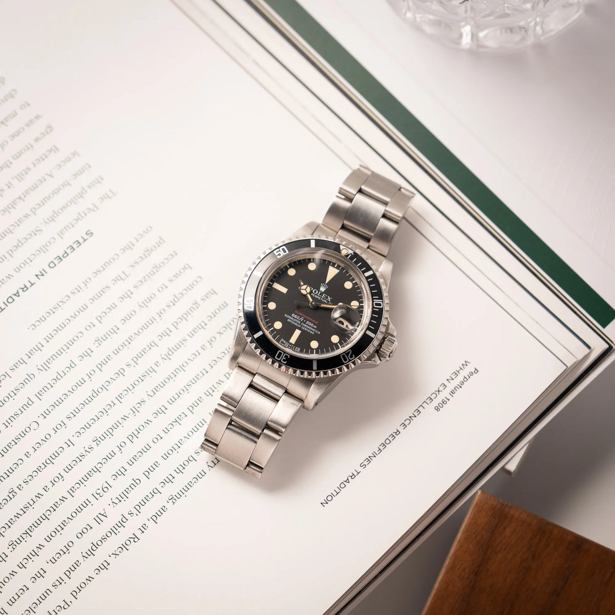 Rolex Submariner Date 1680 mit dem Submariner Red Schriftzug auf dem Mark V Zifferblatt mit schöner gleichmäßiger Patina bei den Zeigern und Indizes liegt auf einem Uhrenmagazin