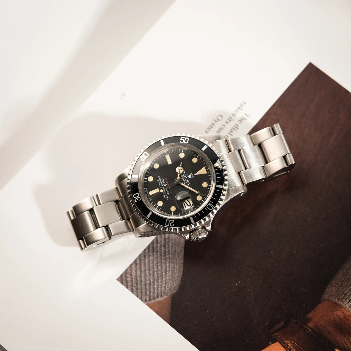 Rolex Submariner Date 1680 mit dem Submariner Red Schriftzug auf dem Mark V Zifferblatt mit schöner gleichmäßiger Patina bei den Zeigern und Indizes liegt auf einem Uhrenbuch