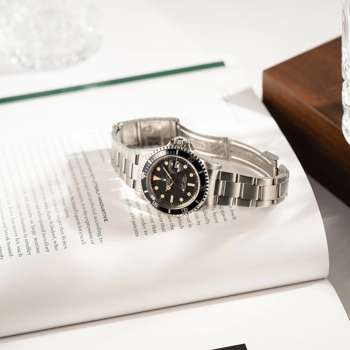 Rolex Submariner Date 1680 mit dem Submariner Red Schriftzug auf dem Mark V Zifferblatt mit schöner gleichmäßiger Patina bei den Zeigern und Indizes liegt auf einem Uhrenbuch