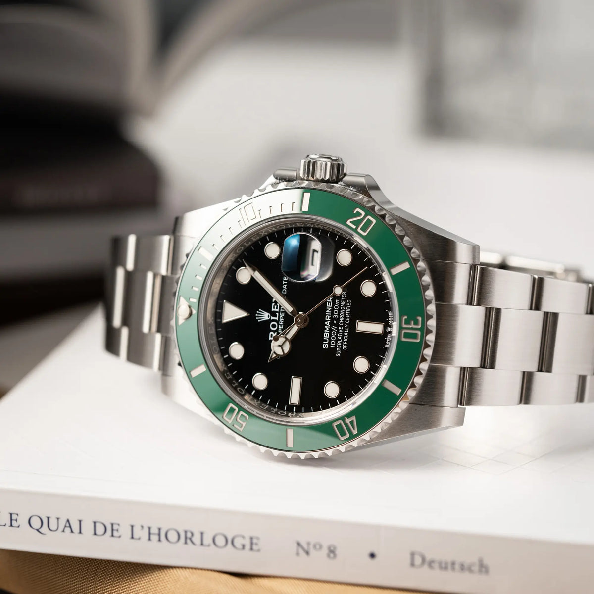 Rolex Submariner Date Starbucks der Referenz 126610LV im 41mm Oyster-Case mit der typischen grünen Keramik-Lünette liegt seitlich auf dem Uhrengehäuse 