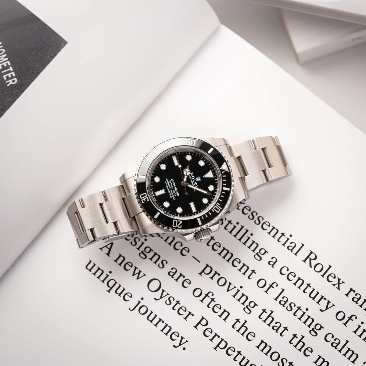 Rolex Submariner No Date der Referenz 124060 mit schwarzem Zifferblatt und schwarzer Keramik-Lünette an einem Oytser-Stahlband im Neuzustand liegt flach auf einem Uhrenbuch