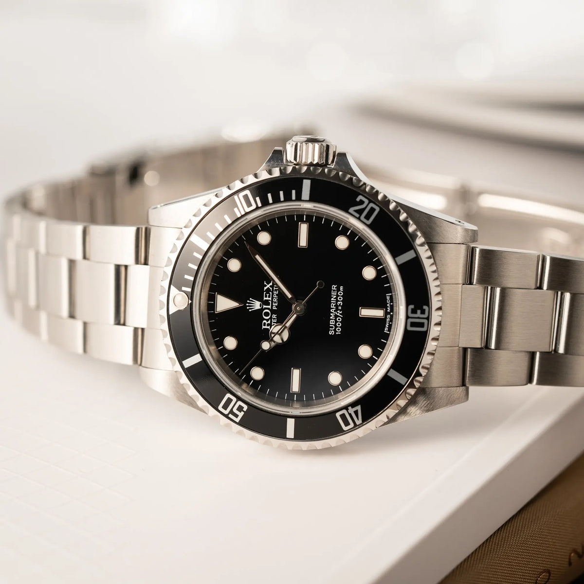 Produktfotografie der seitlich auf dem Uhrengehäuse liegenden Rolex Submariner No Date 14060M mit schwarzem Zifferblatt und der klassischen schwarzen Aluminium-Lünette