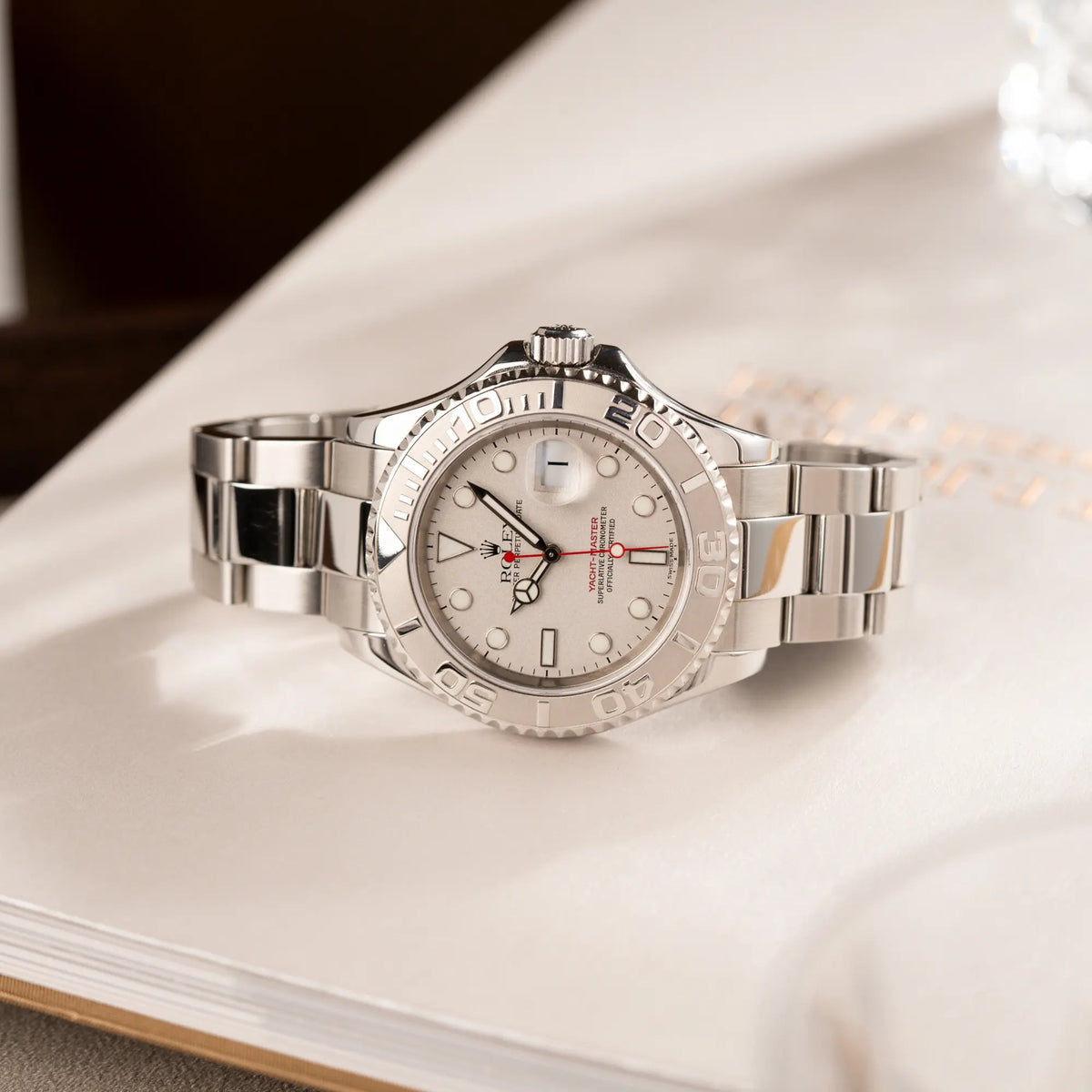 Produktfotografie der seitlich auf dem Gehäuse liegenden Rolex Yachtmaster 40 Platinum mit der Referenz 16622 mit Platin-Lünette und dem typischen roten Sekundenzeiger