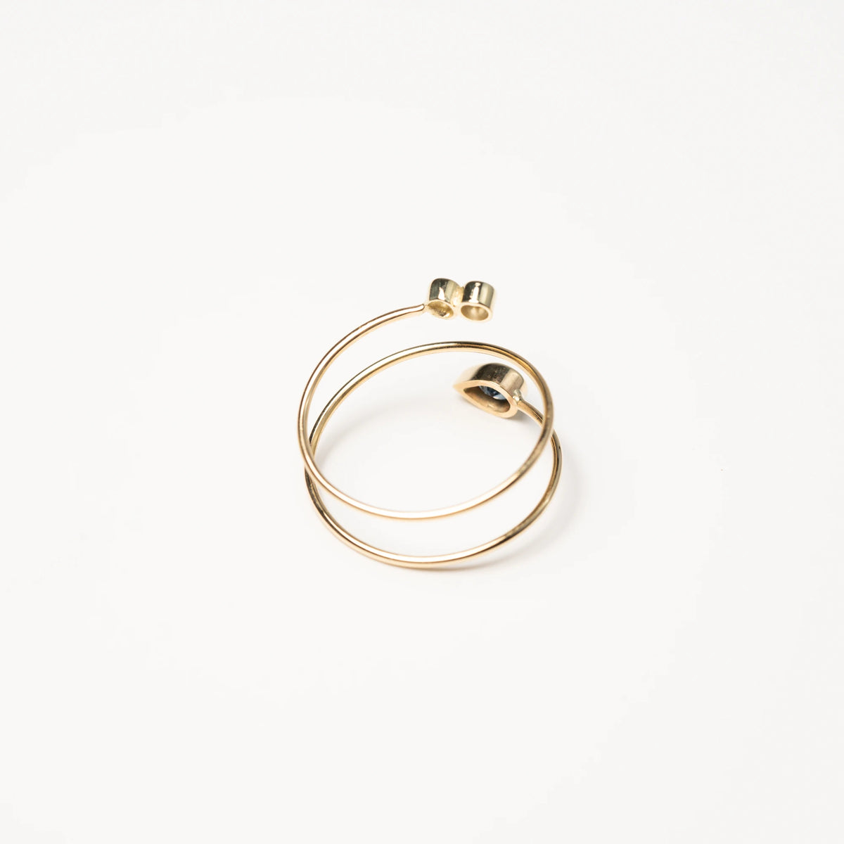 Detailaufnahme des Gelbgoldrings Twisted, der an eine Spirale erinnert und als Blickfang zum Abschluss einen Saphir in Tropfenform und zwei Brillanten verbaut hat, welche die Fassungen der Edelsteine genauer zeigt